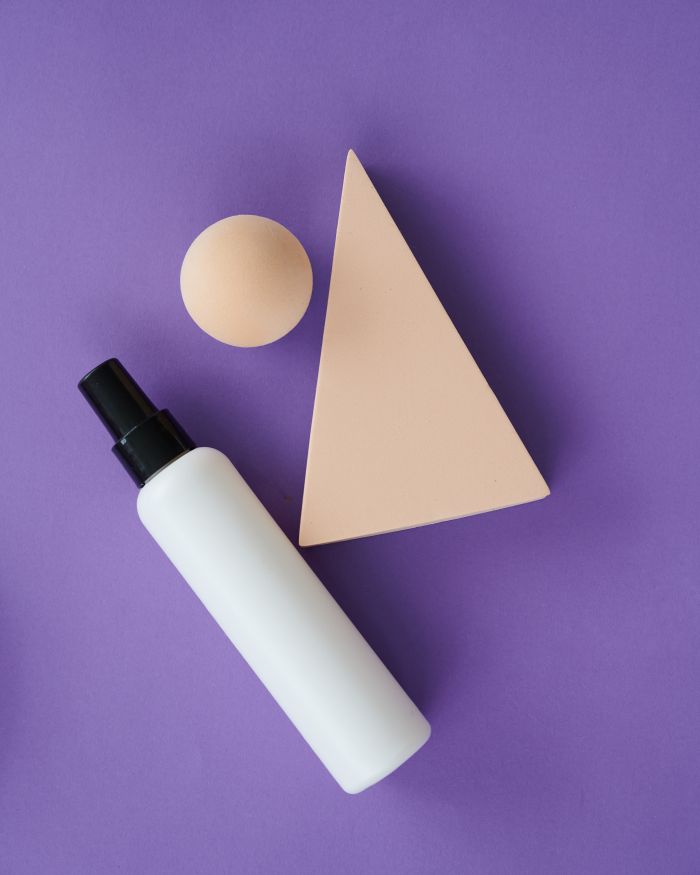 Flatlay of a white spray bottle with geometric shapes on a purple background.